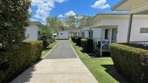 A row of mobile homes with a paved walkway between them, surrounded by well-maintained hedges and grass. - Chinchilla Motor Inn (Chinchilla)
