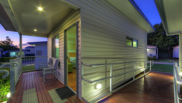 A covered outdoor area with a wooden deck, a metal railing, and a door leading to a building. - Chinchilla Motor Inn (Chinchilla)