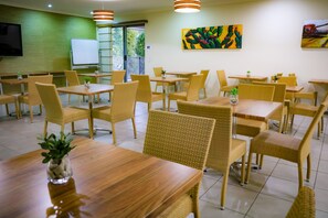 Un comedor con sillas de mimbre y mesas de madera, una pizarra y obras de arte en las paredes.