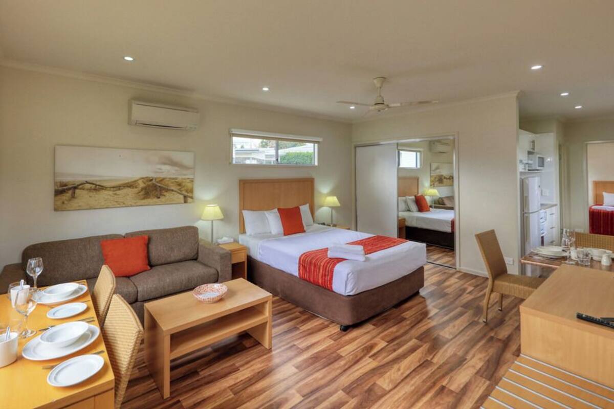 Habitación de hotel con cama, sofá, mesa de comedor con platos y vasos, televisión y ventana.