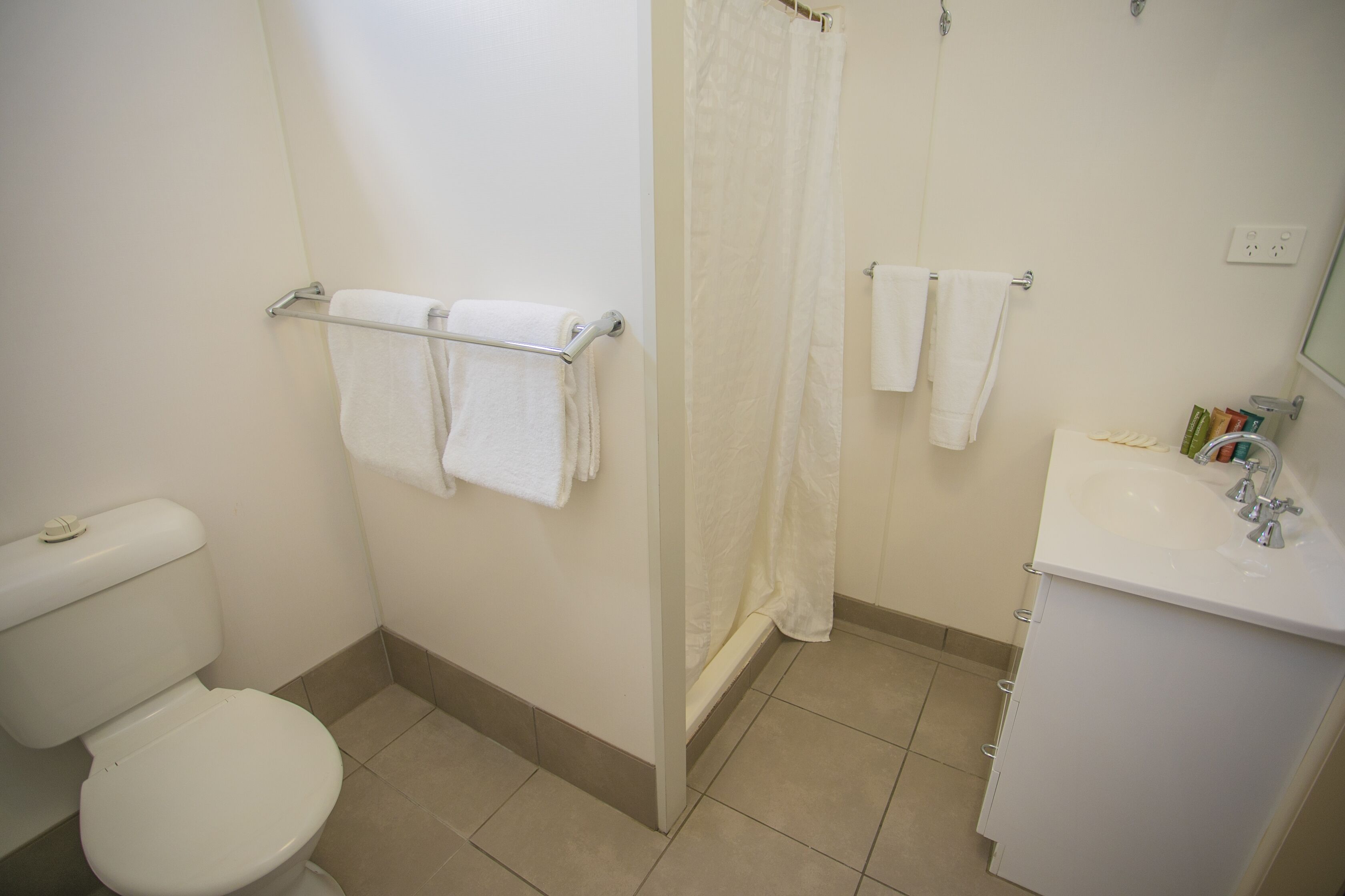 A bathroom with a toilet, a shower with a curtain, and a sink with a mirror.