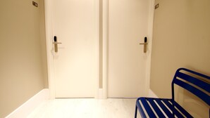 Um quarto com duas portas fechadas, um banco e um chão de cor clara.
