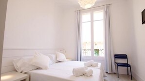 Quarto de hotel com uma cama, uma cadeira e uma janela com cortinas.