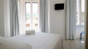 Habitación de hotel con cama, televisión en la pared y vista al balcón exterior.