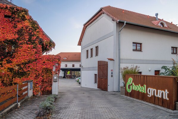 A hotel entrance with a sign reading "Hotel Grunt," a paved driveway, and a building with a tiled roof. - Hotel Grunt (Kosmonosy)