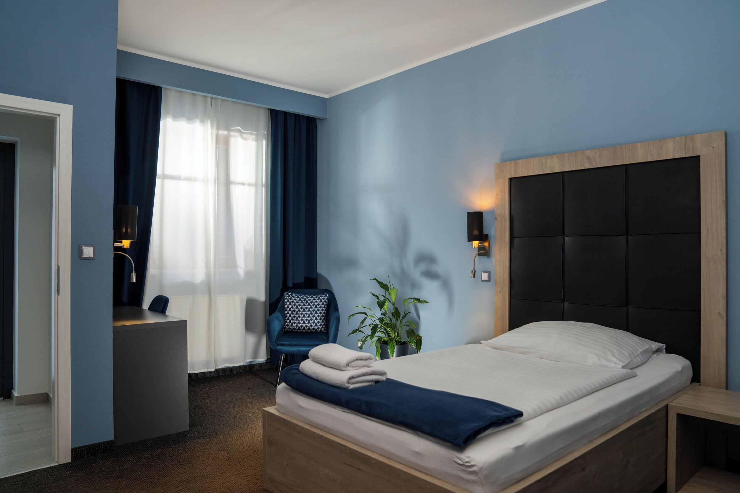 Una habitación de hotel con cama, escritorio, silla y una planta en maceta.