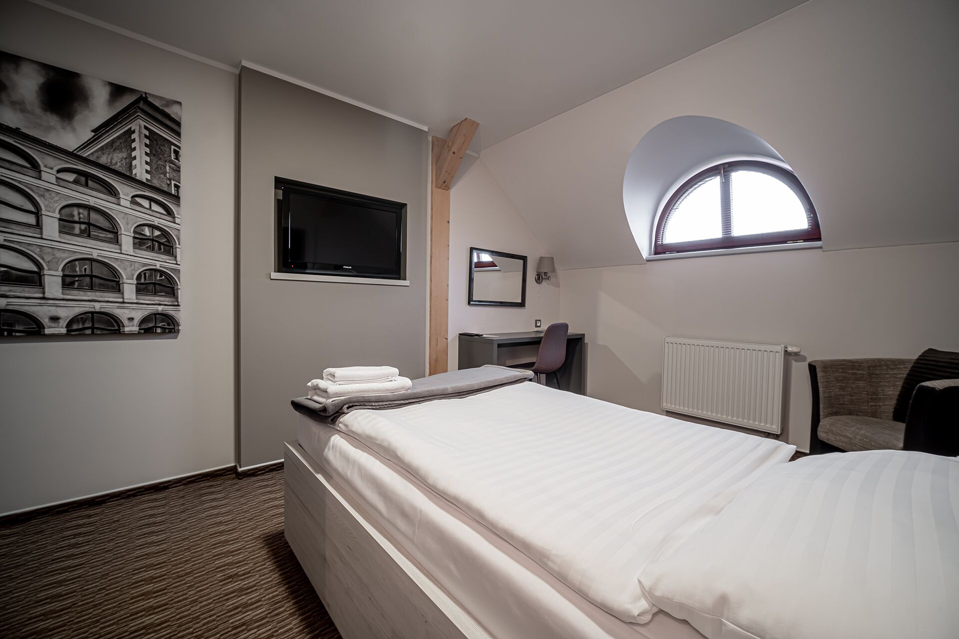 A hotel room with a bed, a desk, a chair, a TV, a window, and a wall-mounted picture.