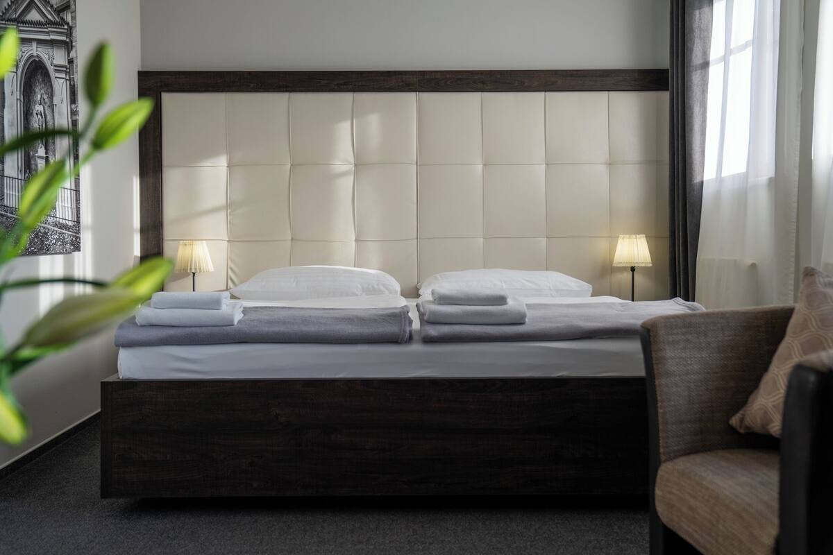 A double bed with a padded headboard, two bedside lamps, and a chair with a cushion.