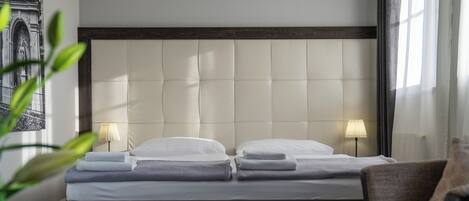 A double bed with a padded headboard, two bedside lamps, and a chair with a cushion.