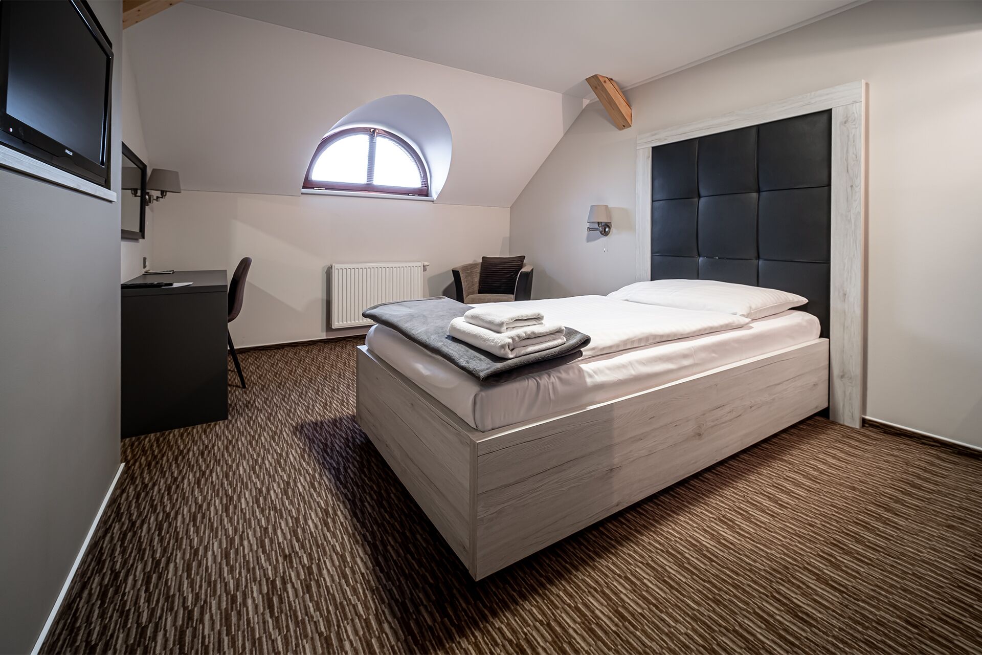 A bedroom with a bed, a desk, a chair, a radiator, and a window.