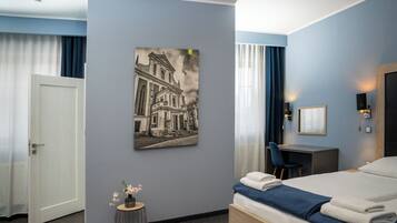 Habitación de hotel con cama, escritorio, silla, una mesita con flores y un cuadro colgado en la pared.
