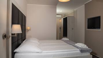 Une chambre d’hôtel moderne avec un grand lit, une lampe de chevet, un téléviseur à écran plat et un lit parfaitement fait, agrémenté de serviettes.