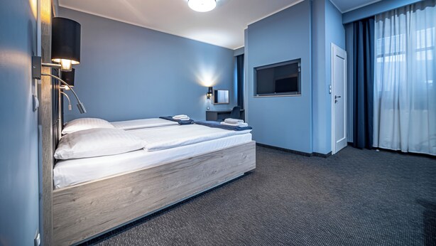 Una habitación de hotel con una cama de madera, un televisor de pantalla plana, un escritorio con una silla y un amplio ventanal con cortinas.