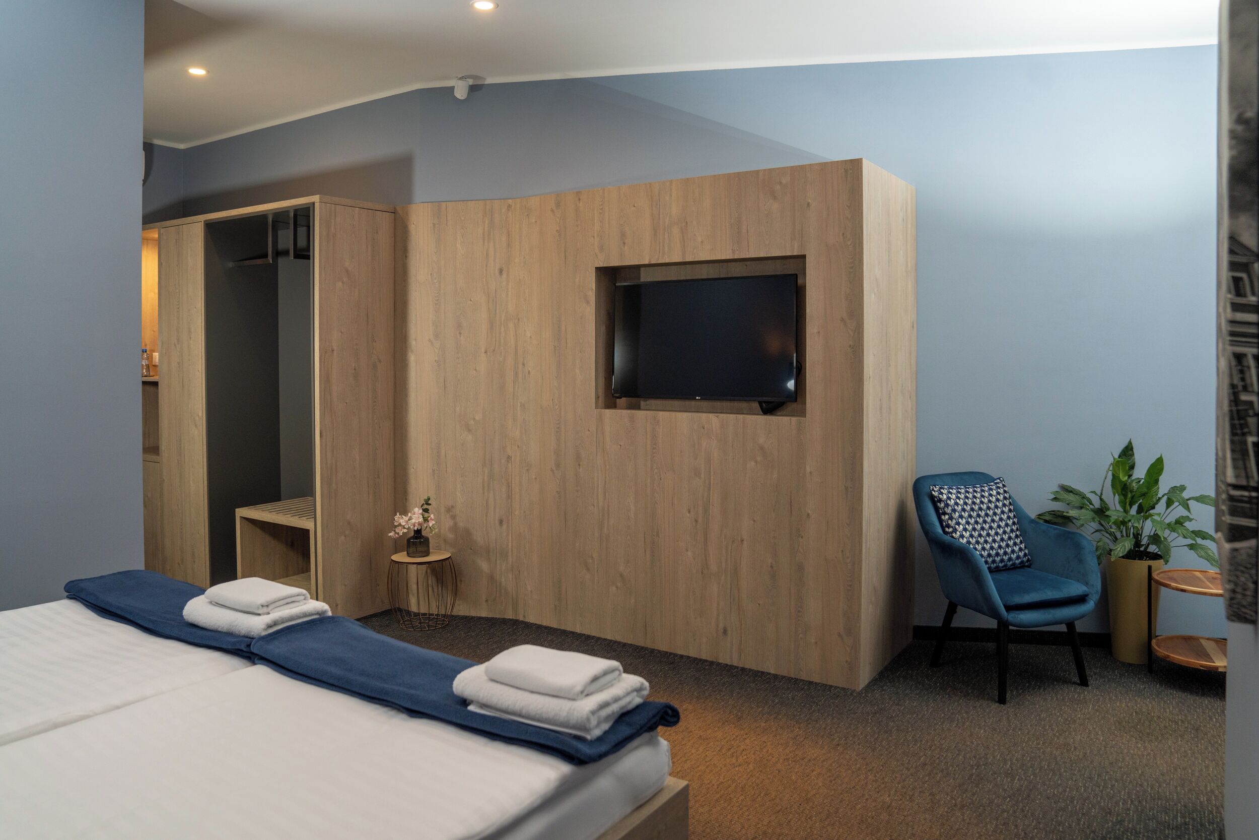 Una habitación de hotel moderna con una cama, un televisor montado en la pared, una zona de estar con una silla y una mesita.