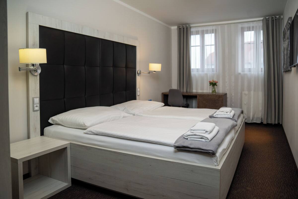 A hotel room with a large bed, bedside tables, a desk, and a chair.