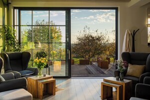 Una sala de estar moderna con un amplio ventanal corredera que da a una terraza exterior, amoblada con sofás y una mesa de centro.