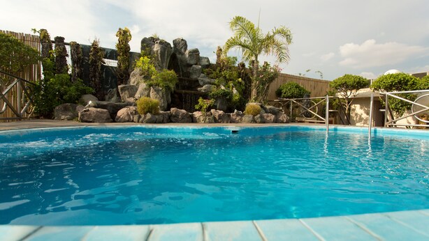 A swimming pool with clear blue water, surrounded by rocks and greenery, and a wooden fence in the background. - Hotel Benilde Maison De La Salle (Manila)