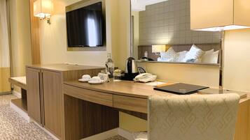 Quarto de hotel com escrivaninha de madeira, uma cadeira, televisão na parede, espelho e cama com colcha estampada.
