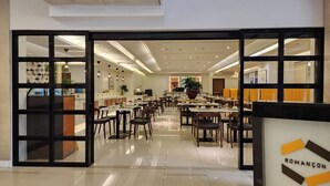 A spacious dining area with multiple tables and chairs, a large potted plant, and a sign reading "ROMANÇON". - Hotel Benilde Maison De La Salle (Manila)