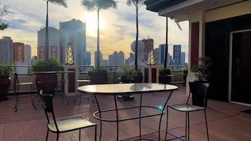 Terraço no terraço com vista para o horizonte urbano, apresentando uma mesa redonda e cadeiras, plantas em vasos e um design arquitetônico moderno.