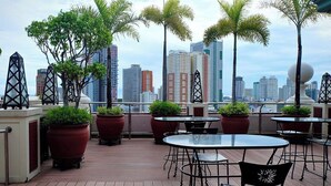 A rooftop terrace with tables and chairs, potted plants, and a city skyline in the background. - Hotel Benilde Maison De La Salle (Manila)
