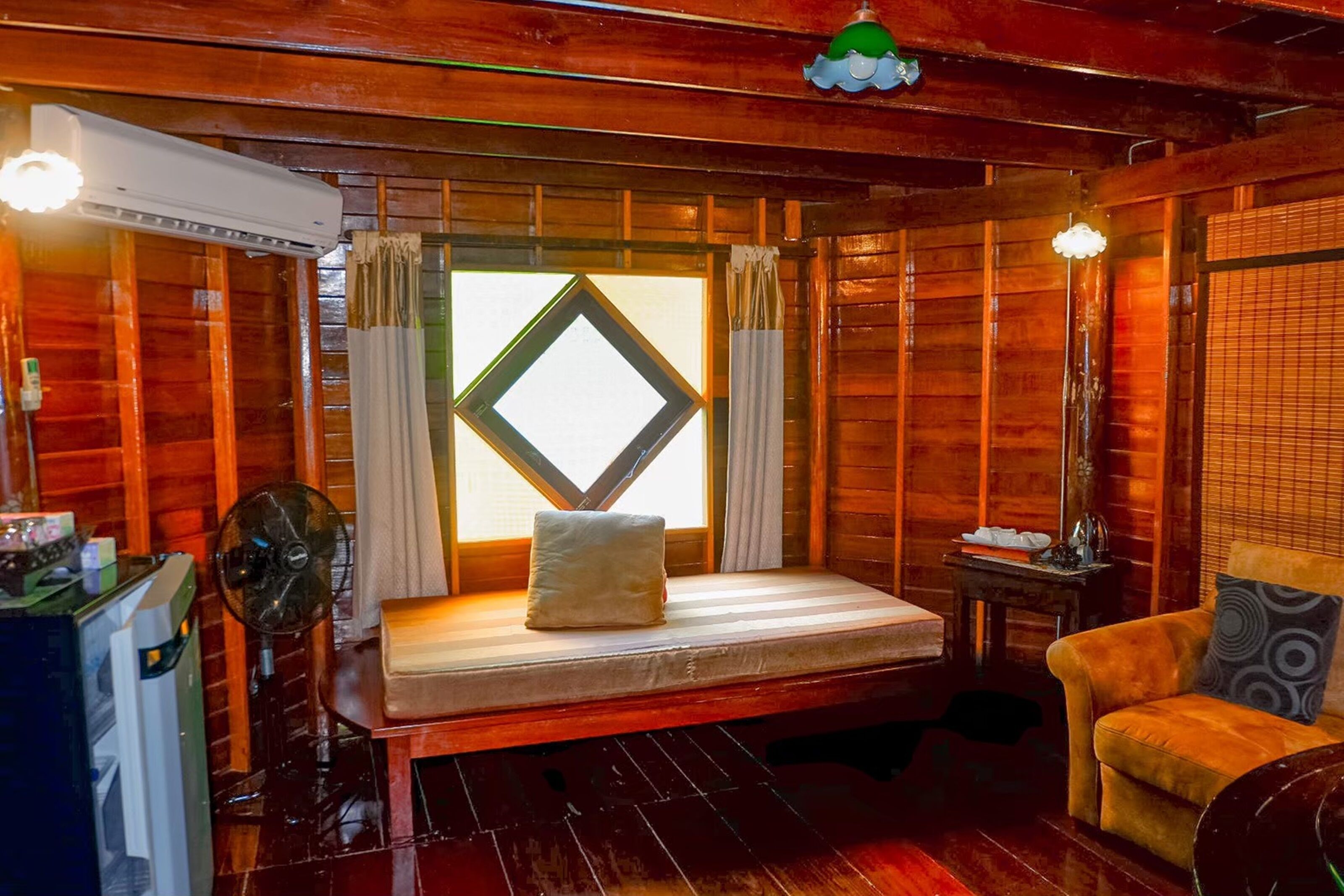 A wooden room with a bed, a chair, a table, and a fan.