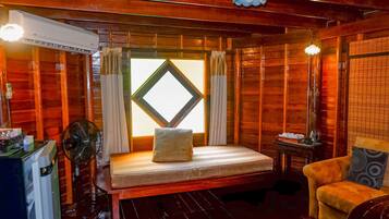 A wooden room with a bed, a chair, a table, and a fan.
