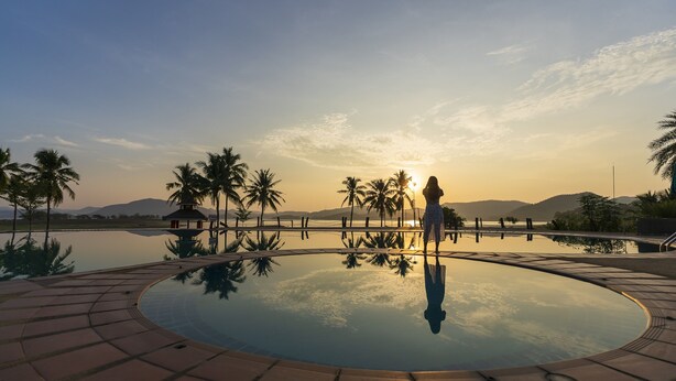 Una piscina infinita circular con palmeras y vistas a las montañas al atardecer.