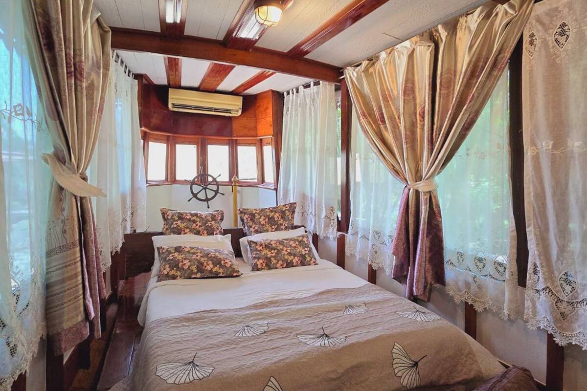 Un dormitorio rústico y acogedor con techo de madera, cama con ropa de cama floral y cortinas.
