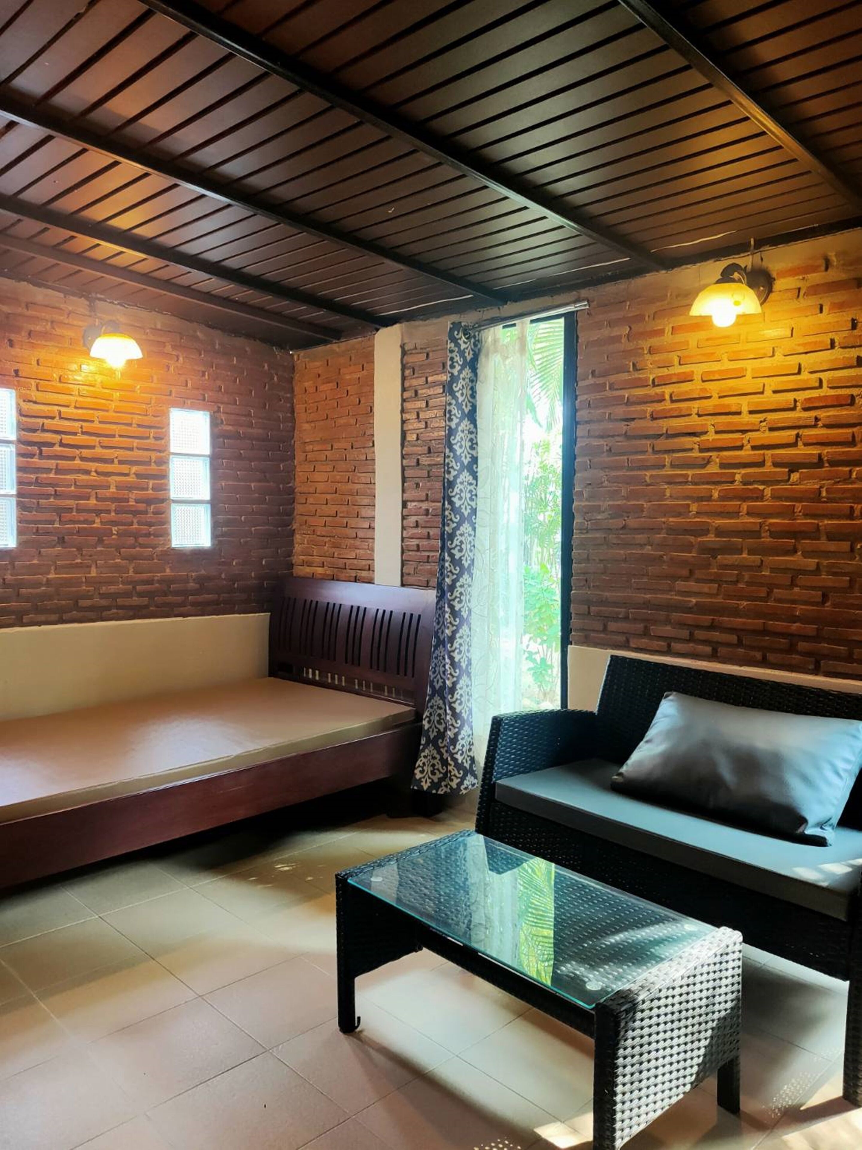 Una habitación acogedora con pared de ladrillo, un banco acolchado, un sofá y una mesa de centro de vidrio.
