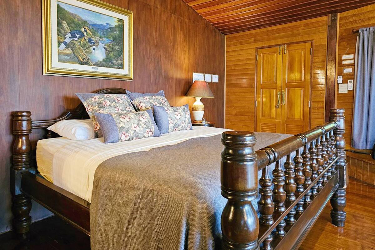 Una habitación con paneles de madera, una cama, un cuadro y un armario de madera.