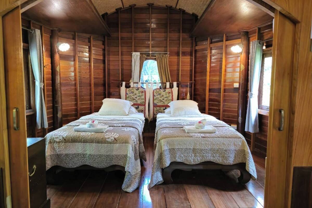 Una habitación tipo cabaña con dos camas, paredes de madera, un ventanal pequeño y un techo con vigas de madera.