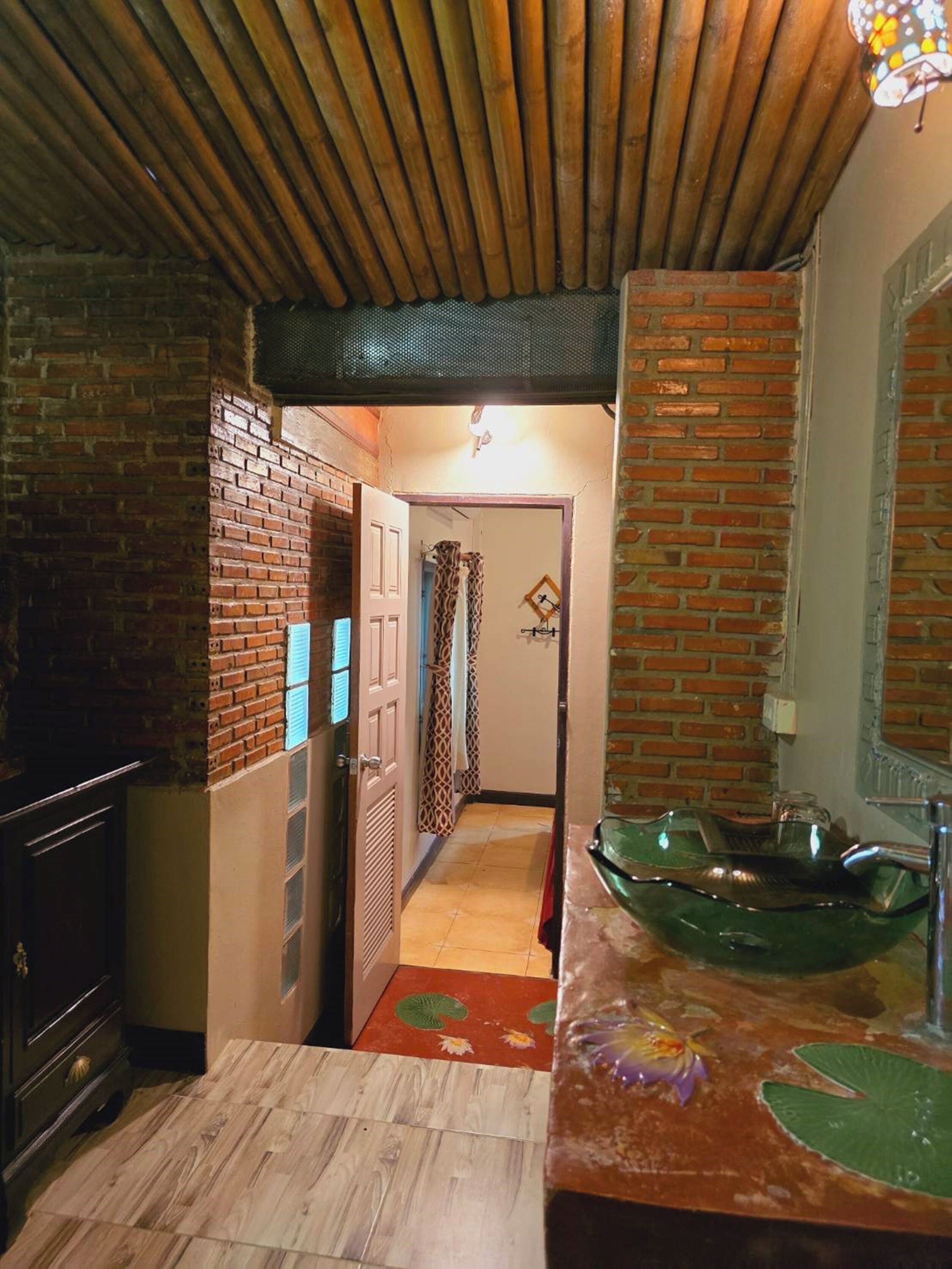 Un estrecho pasillo con techo de madera, pared de ladrillo y un lavamanos de vidrio verde.