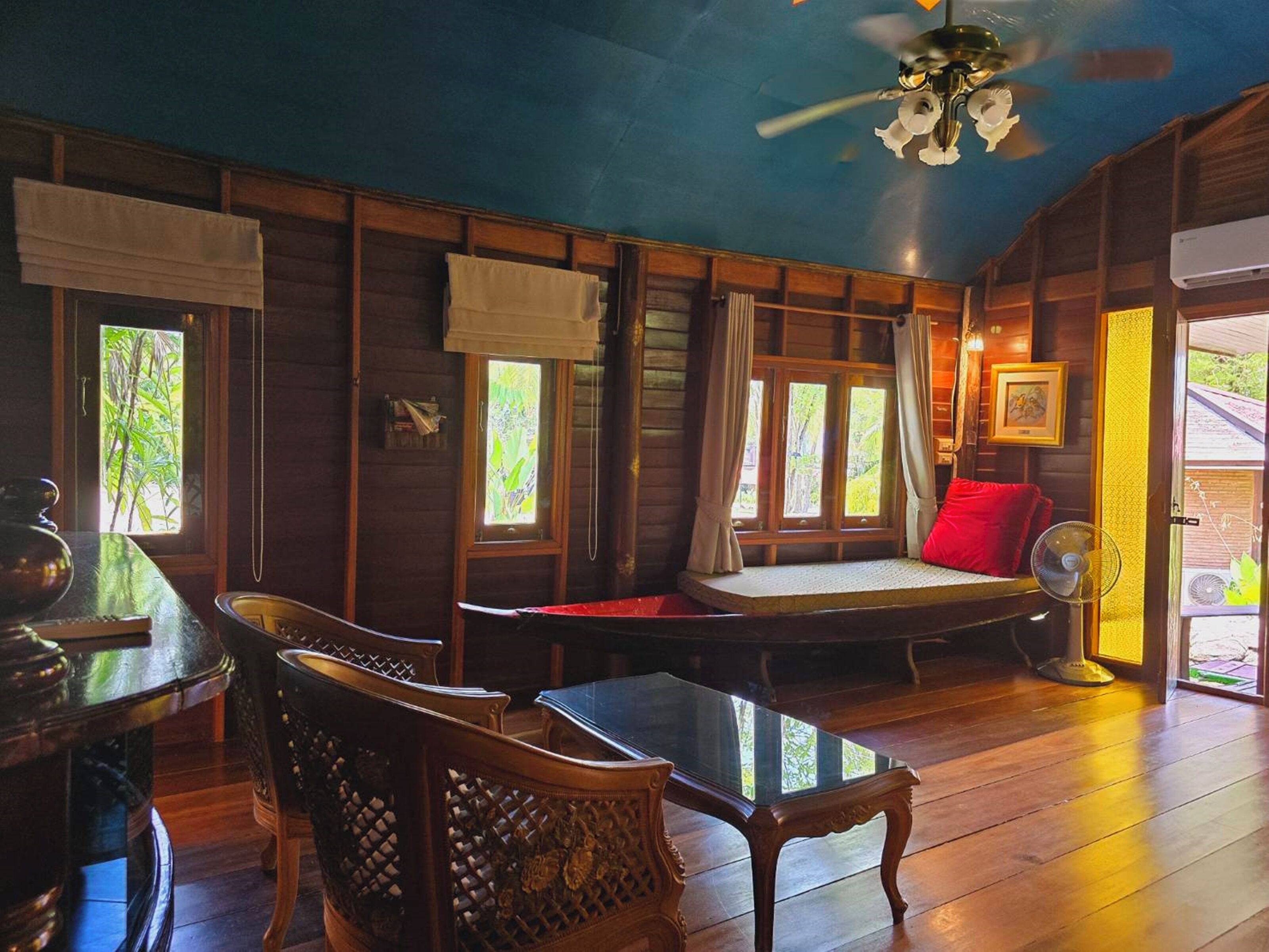A cozy room with wooden walls, a ceiling fan, a bed with a red pillow, a table, and a chair.