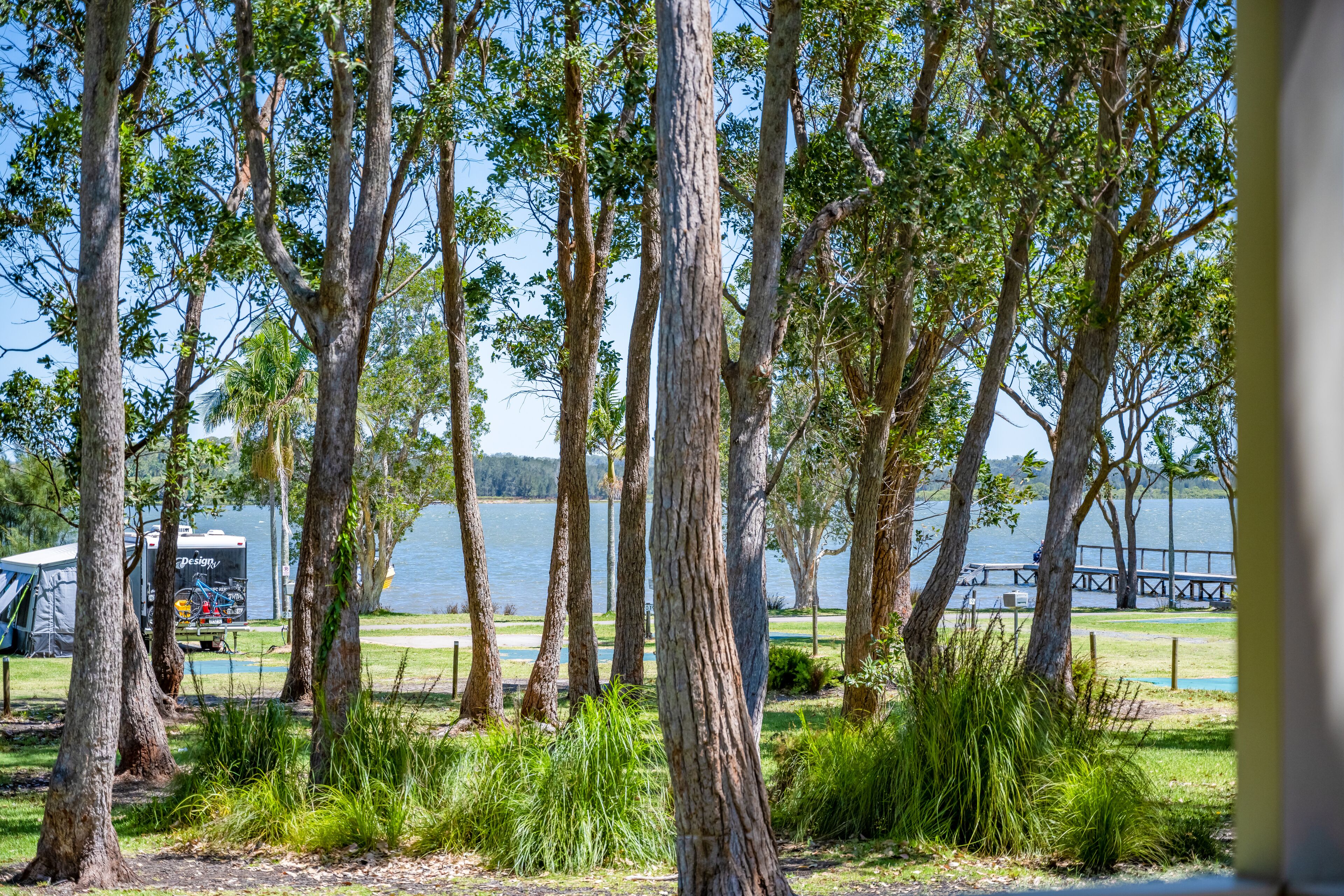 A campsite with tents, a trailer, and a lake view.