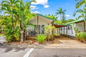 A single-story mobile home with a covered porch, surrounded by tropical vegetation. - Koala Shores Port Stephens Holiday Park (Lemon Tree Passage)