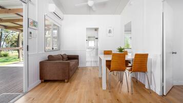 A modern living room with a wooden floor, a brown sofa, a dining table with two chairs, and a ceiling fan.