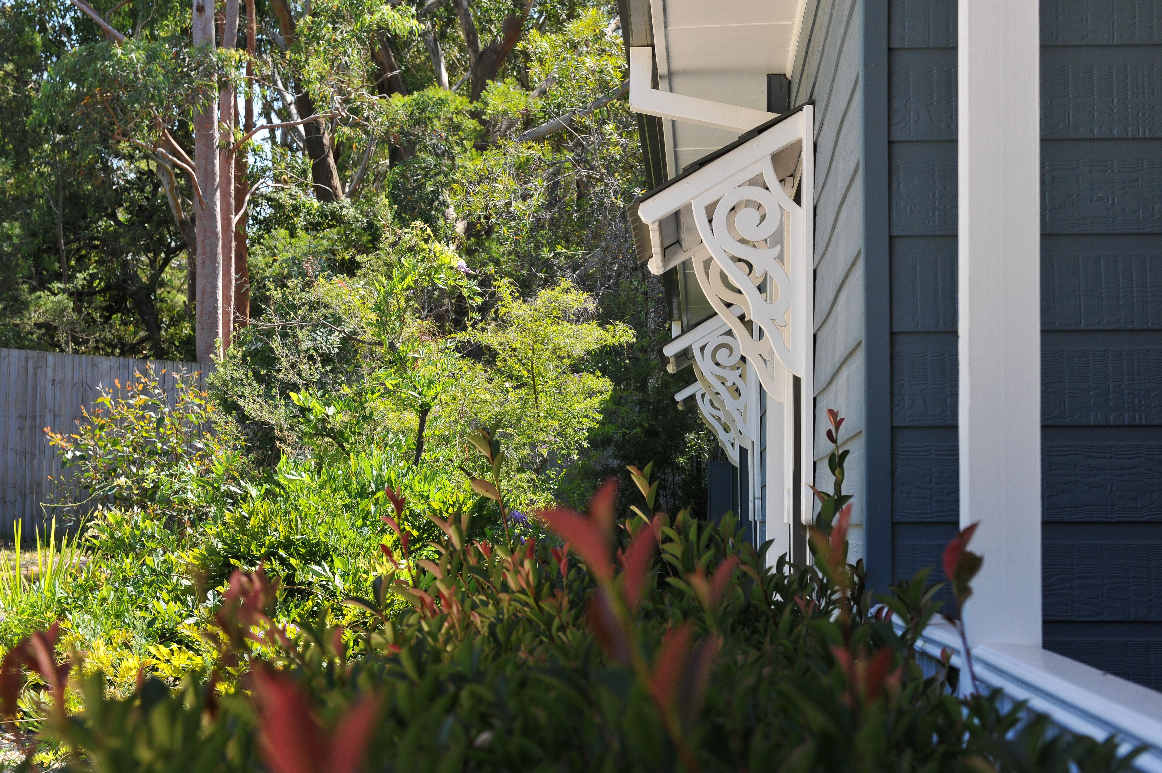 A house with a dark siding exterior, a white decorative railing, and lush greenery in the yard.