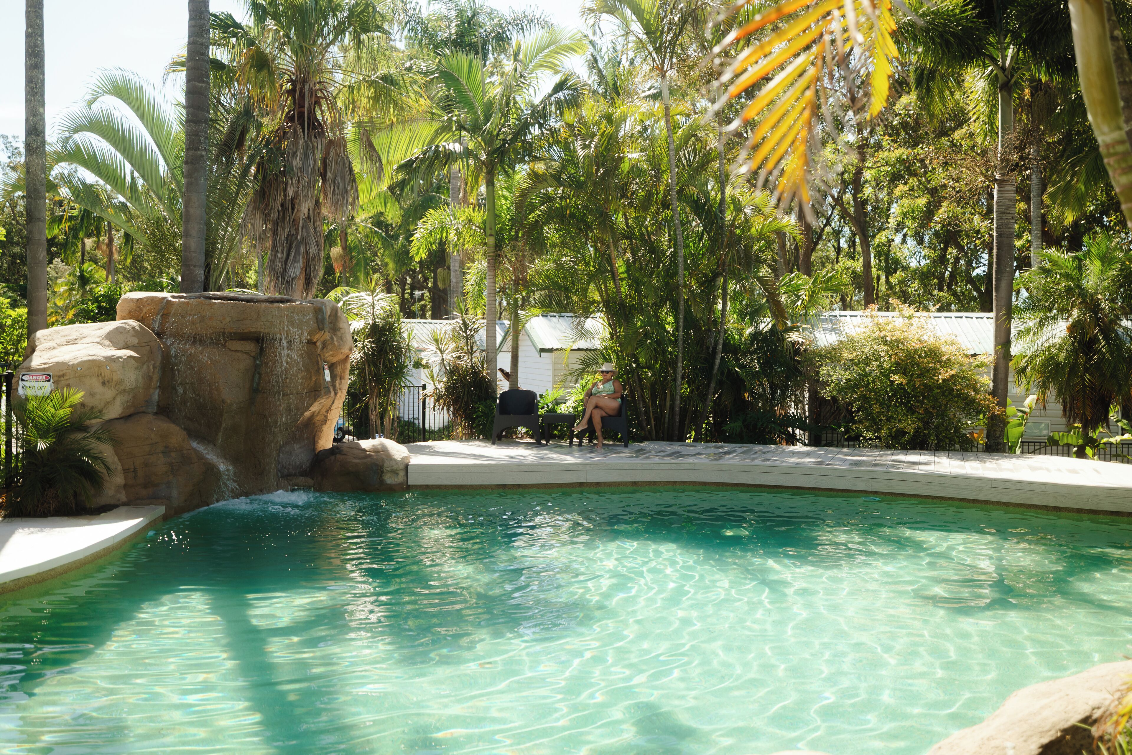 A pool surrounded by palm trees and a white building.