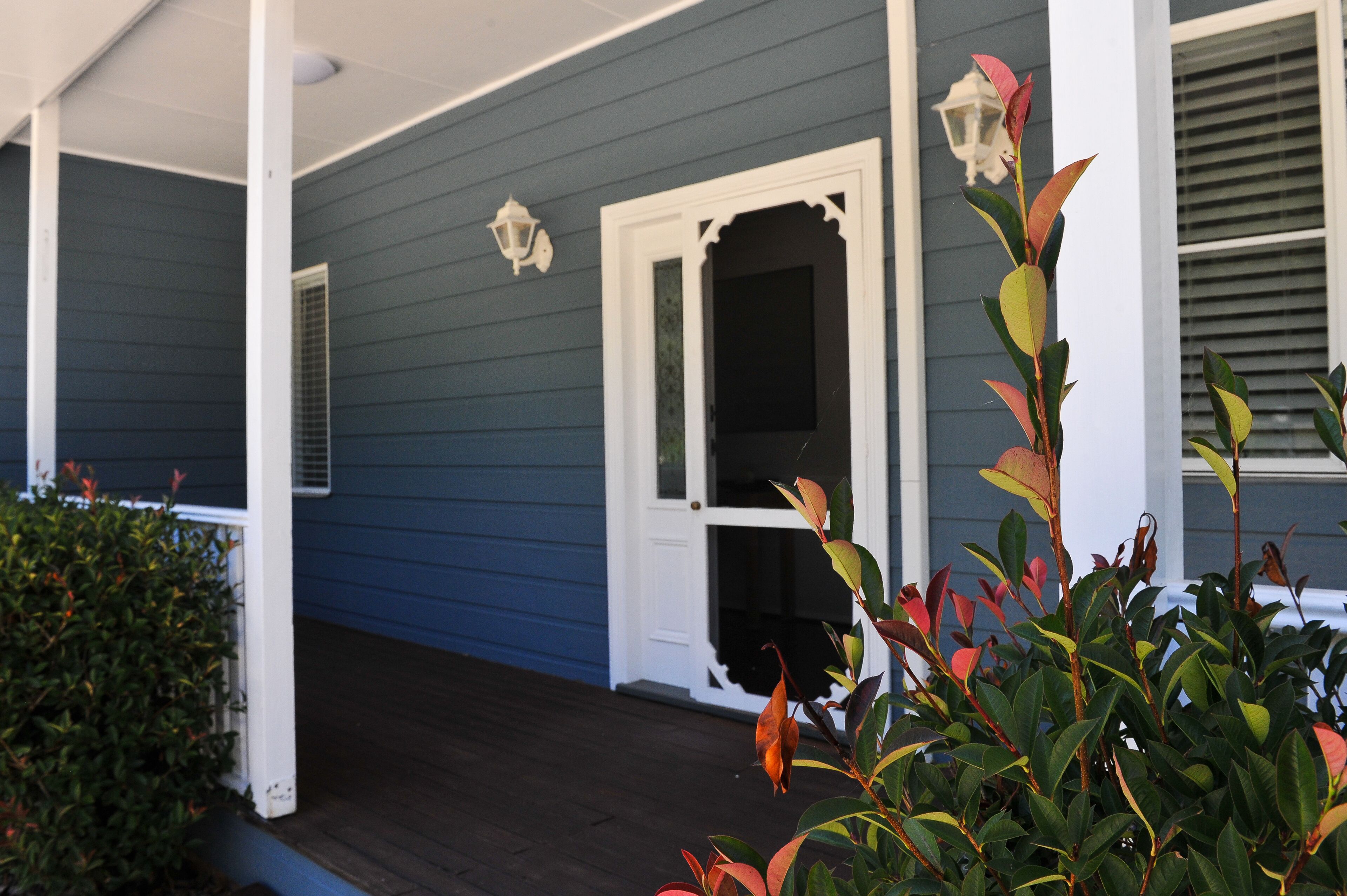 A porch with a dark wooden floor, a white door with glass panels, and a blue exterior wall.