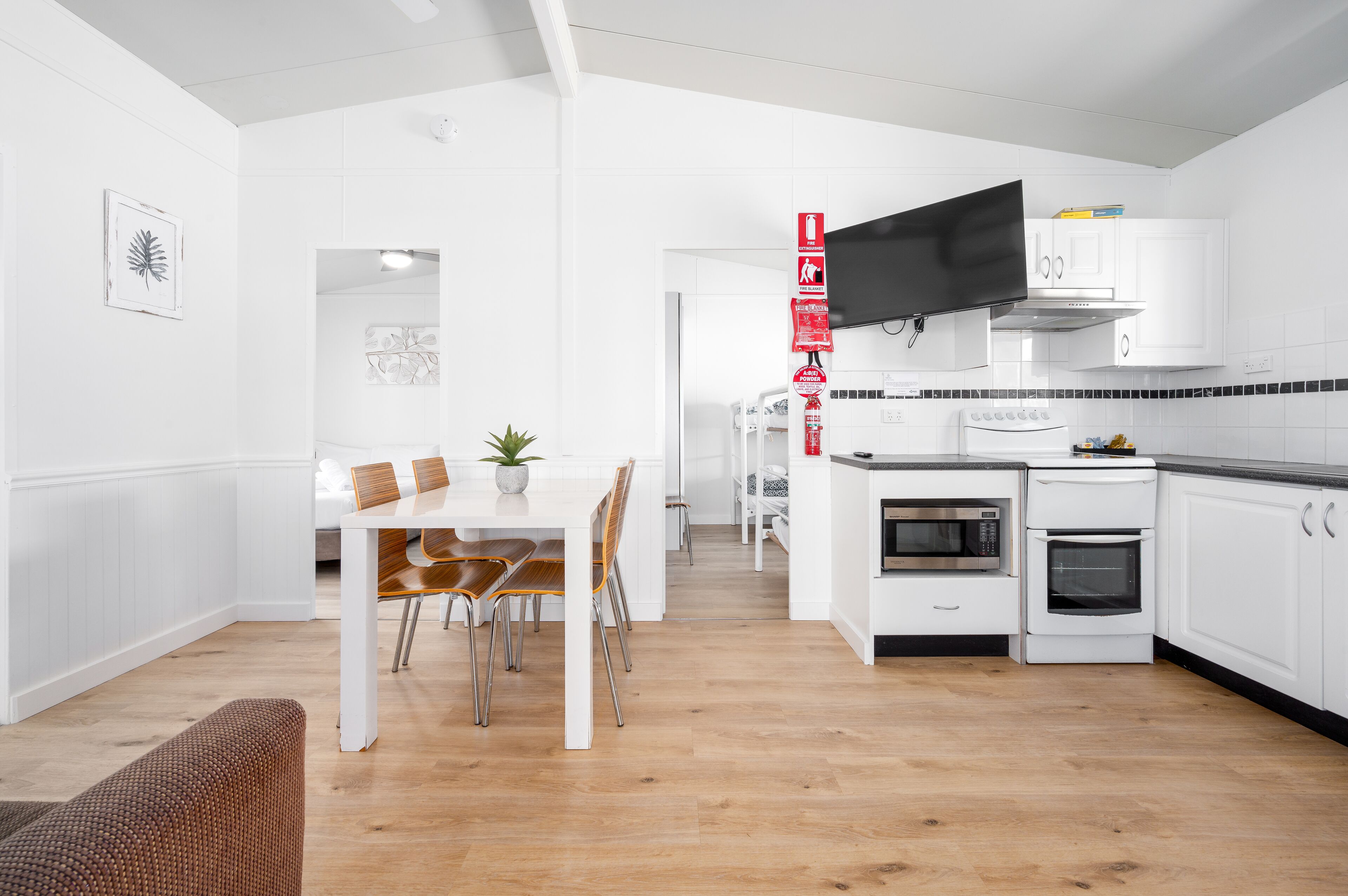 A modern kitchen with white cabinets, a flat-screen TV, and a dining area with a table and chairs.