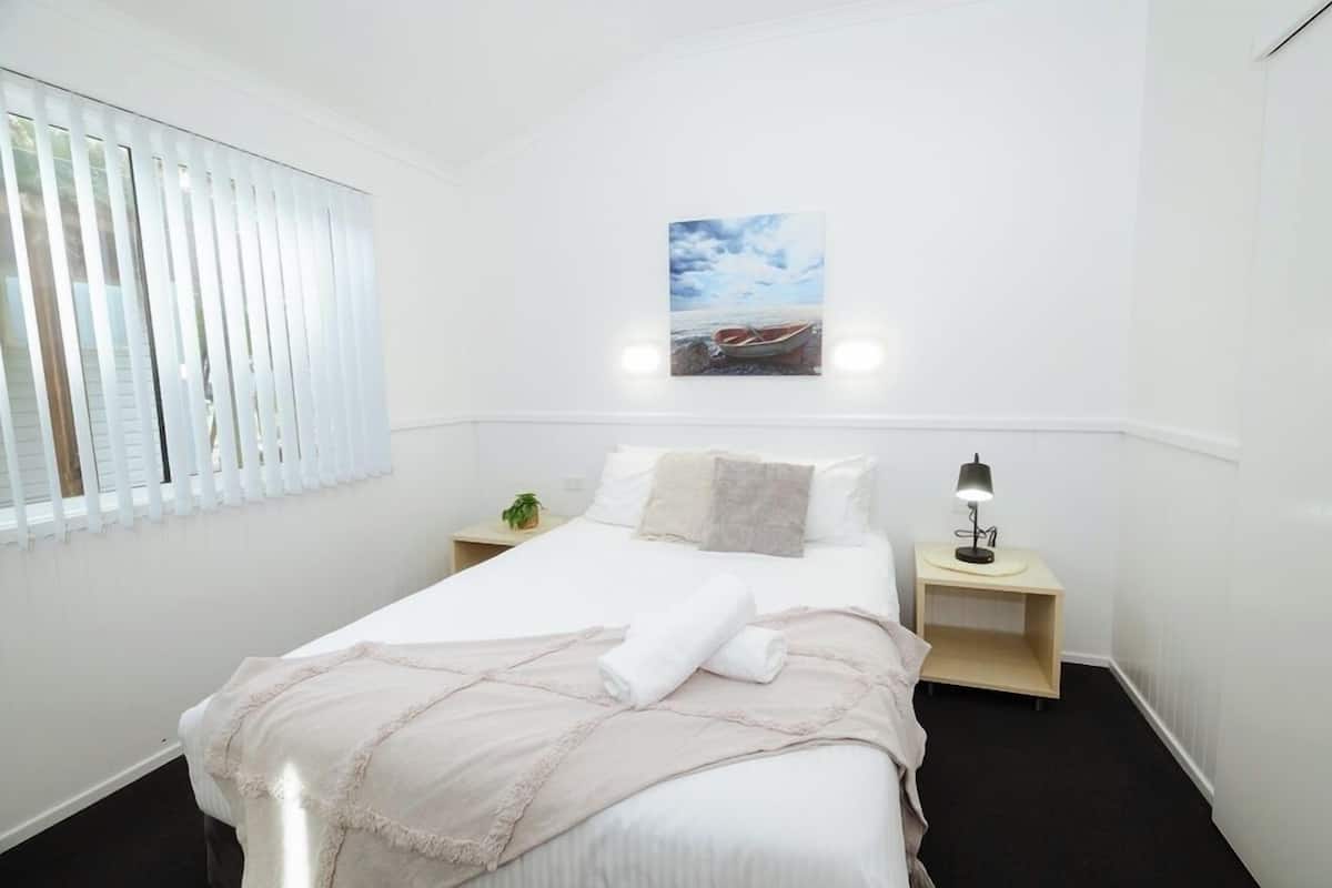 A neatly arranged bedroom with a bed, bedside tables, a wall-mounted picture, and a window with blinds.
