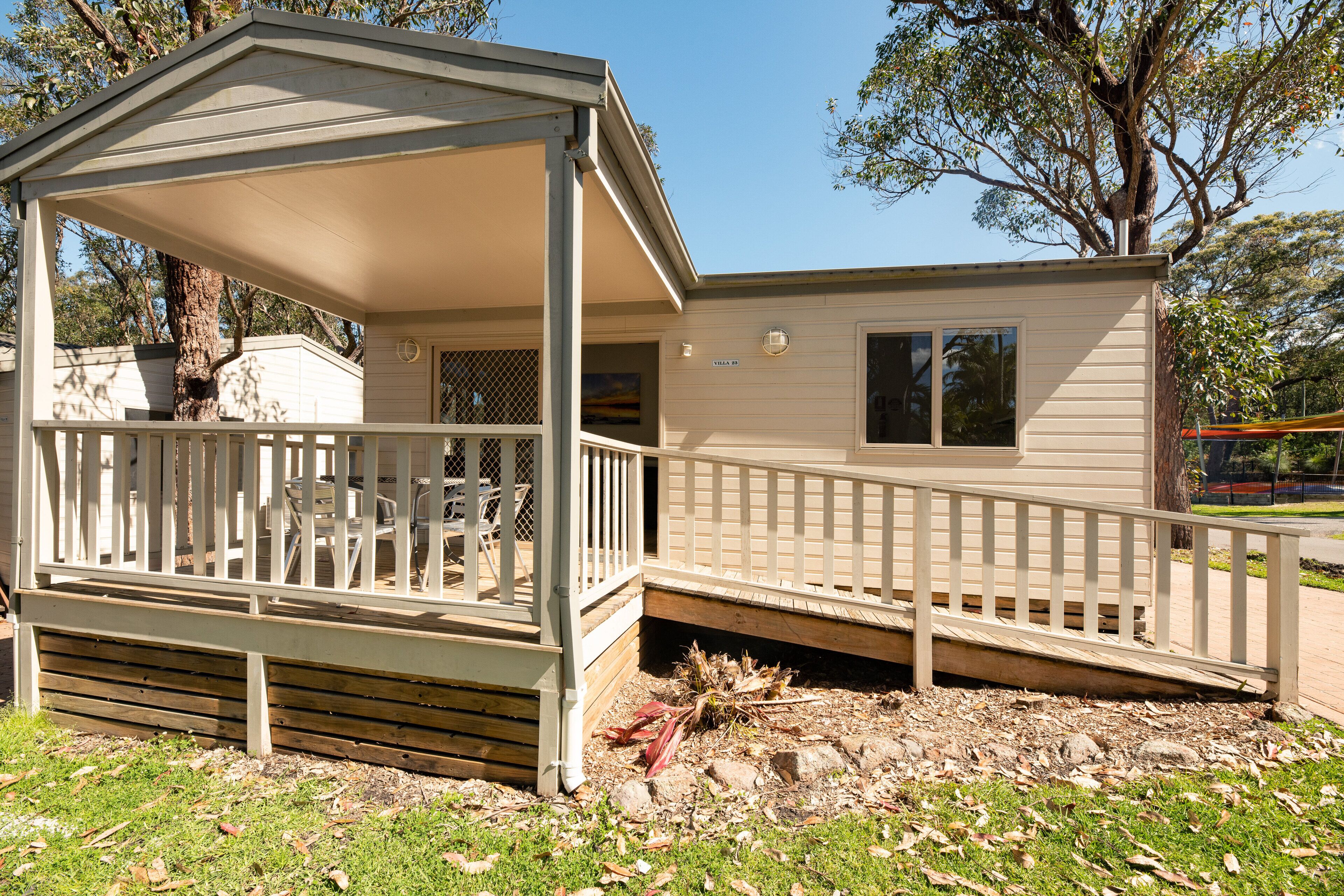 A small, single-story mobile home with a covered porch and a fenced deck area.