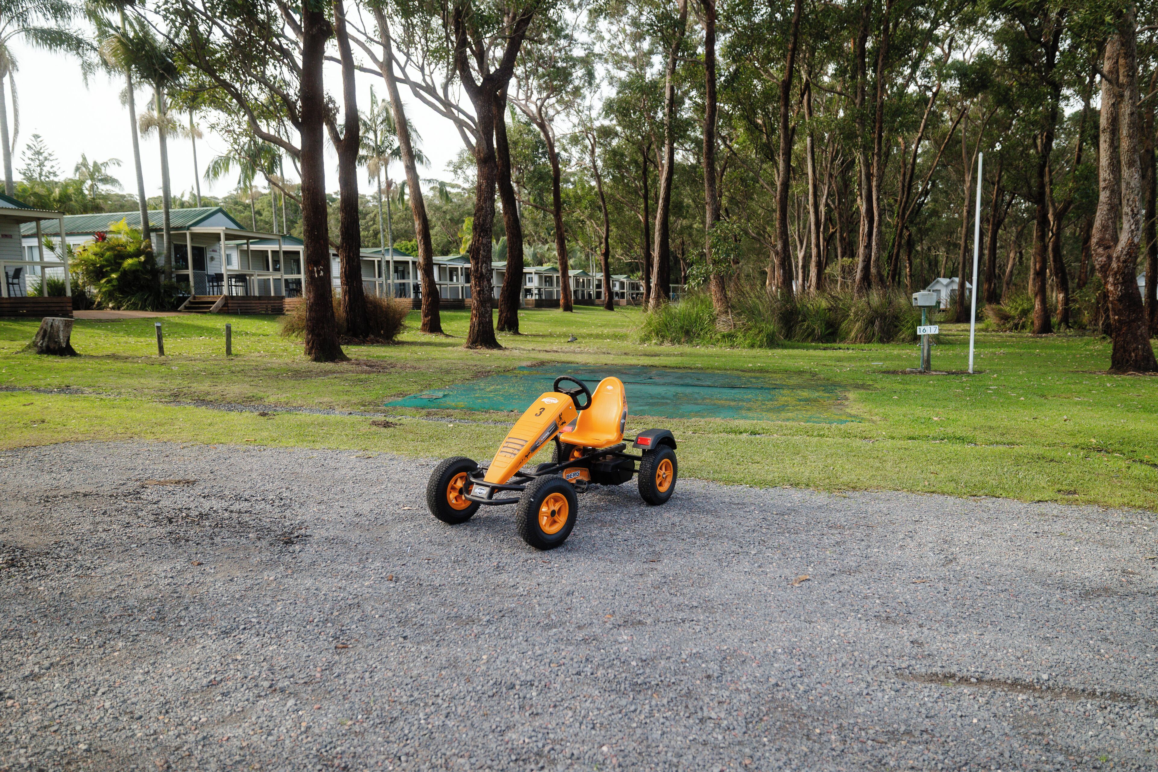 Un kart sobre un camino de grava, con una casa y árboles al fondo.