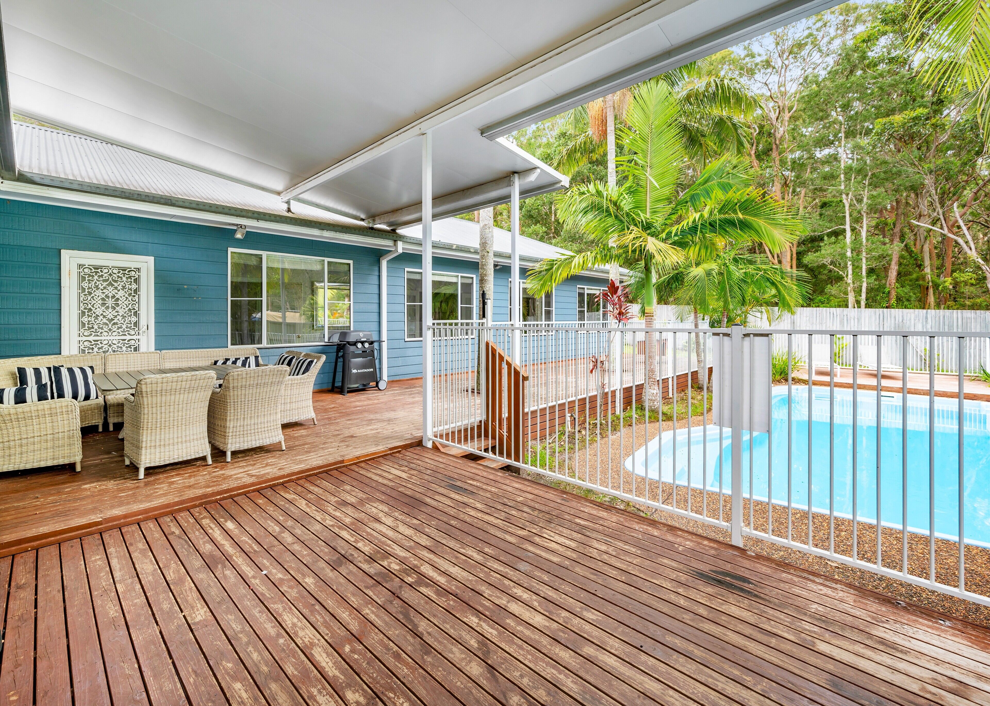 A covered outdoor area with a pool, wooden deck, and seating area.