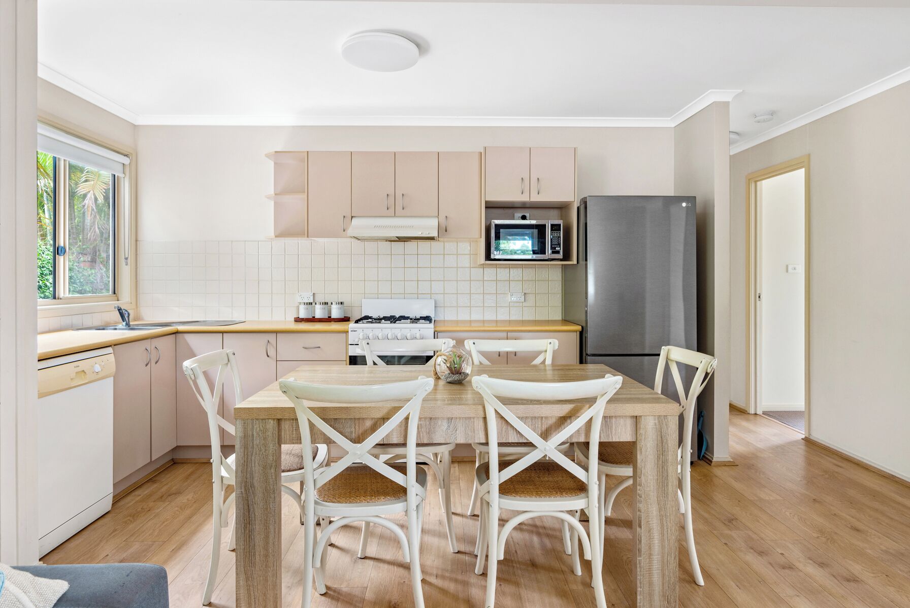 A modern kitchen with white cabinets, a microwave, a stainless steel refrigerator, and a dining table with white chairs.