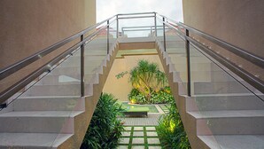 A staircase with glass railings leading to a rooftop garden with plants and a seating area. - O Villas (Keroboken Kelod)