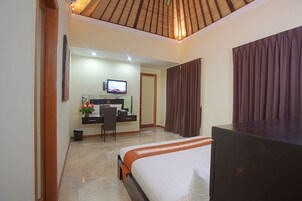 Quarto de hotel com uma cama, uma mesa com computador, televisão e porta de banheiro.
