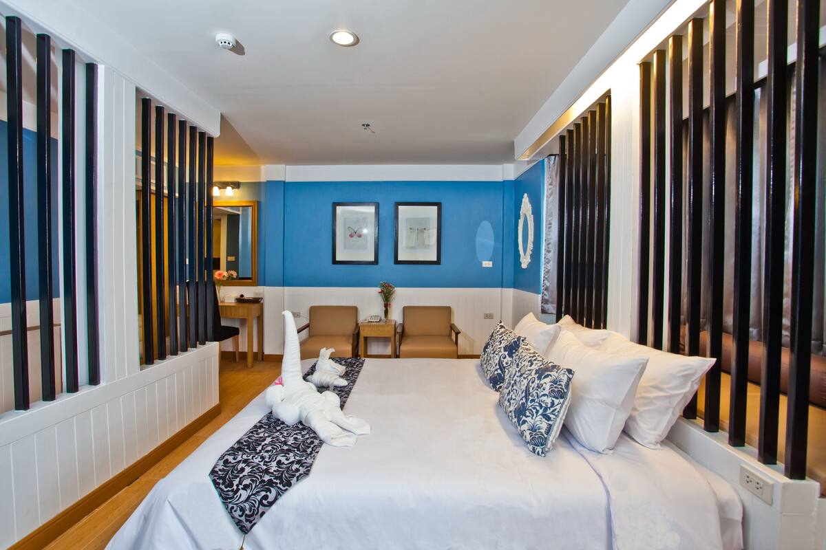 A hotel room with a large bed, two chairs, a desk, and a mirror.