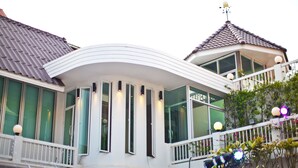 A modern building with a curved balcony, large windows, and a weather vane on the roof. - Paradise Hotel (Udon Thani)